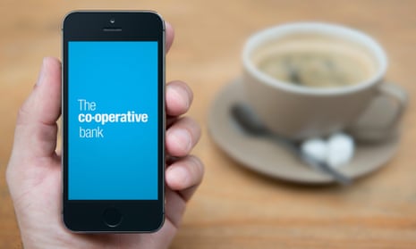 A man looks at his iPhone, which displays the Co-operative bank logo, while sitting with a cup of coffee