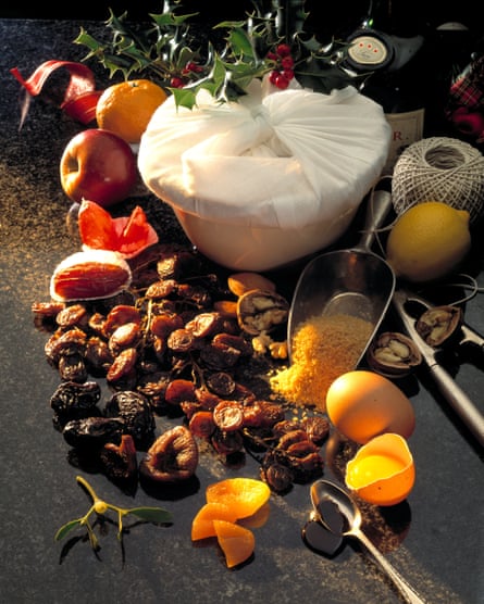 Christmas pudding in basin with a muslin cover on it and other ingredients surrounding it.