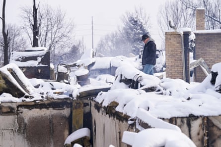A man looks through the snow-covered remains of his brother’s burned home on Saturday.
