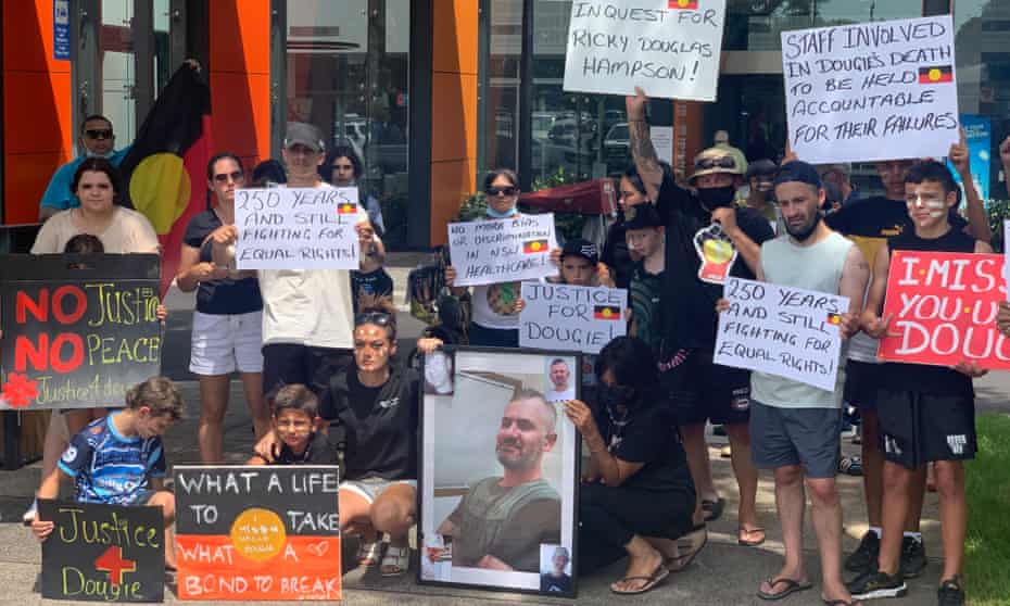 A group of people holding protest signs and pictures of Ricky 'Dougie' Hampson Jr. The signs call for justice, accountability, a coronial inquest etc