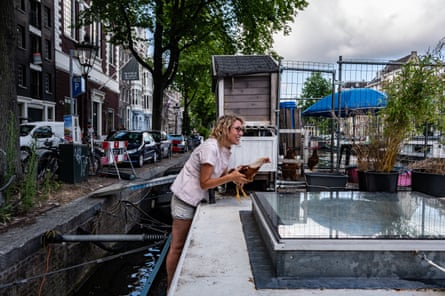 Leentje Schade stands on the side of her houseboat, leaning on the roof, holding a chickren