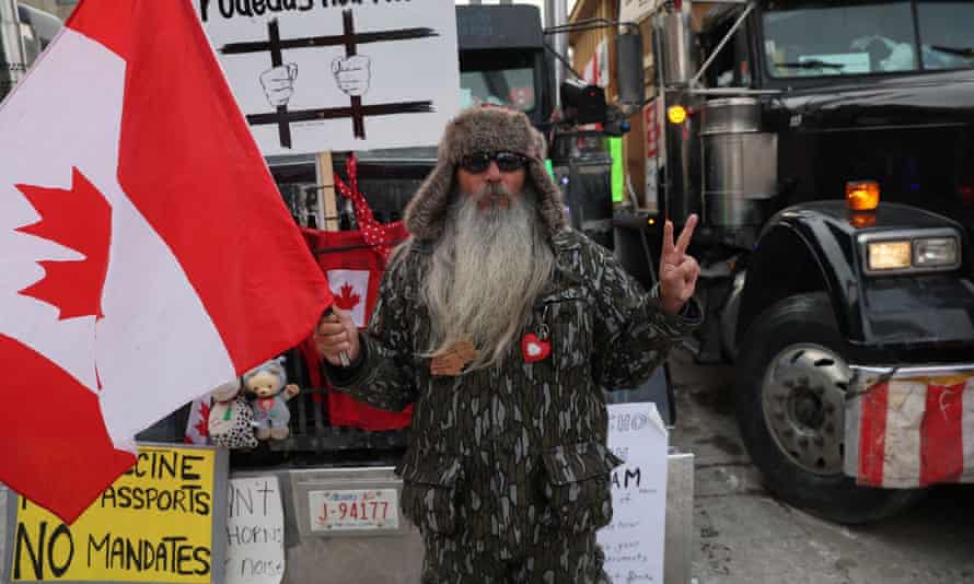 A person stands with a flag next to parked trucks as protests against coronavirus vaccine mandates continue in Ottawa, Canada.