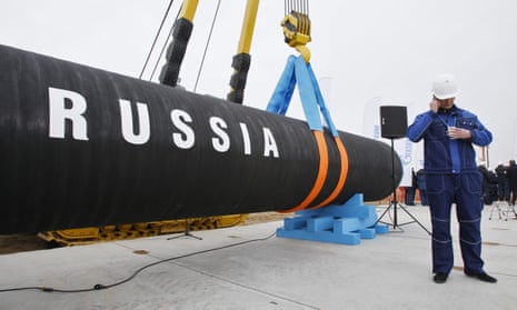A construction worker speaks on the phone next to a huge black gas pipe with RUSSIA written in white on it