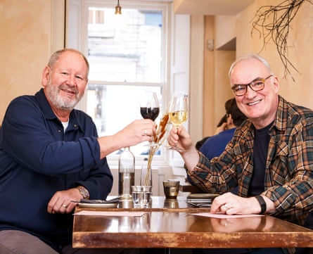 Geoff and Terry clinking wine glasses at a restaurant table and smiling at the camera
