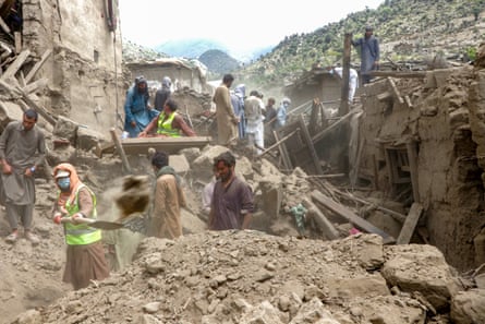 A group of men can be seen in the rubble of homes. One shovels earth on to a large pile