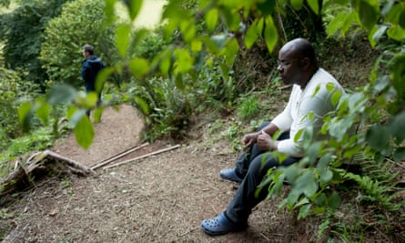 A man sits in contemplation on a bench in a wooded area of The Sharpham Trust retreat in Devon, UK.