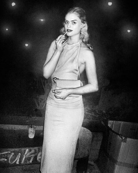 A young woman in a long dress paints her lips as she looks at the camera