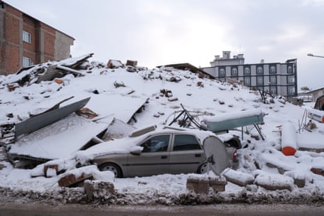 A ruined building and car sit under snowfall in Elbistan.
