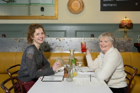 Moira Ruth sitting at a restaurant table holding their drinks and smiling at the camera
