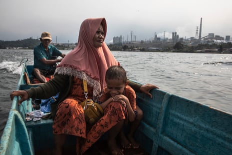 Upin steers his boat with wife Jenni and son Riski past nickel factories in Sulawesi, Indonesia