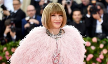 Anna Wintour wearing a light pink feather shawl and large silver necklace on the stairs at The Metropolitan Museum of Art's Costume Institute benefit gala with photographers behind her