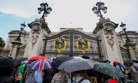 People gather under umbrellas outside Buckingham Palace in London.