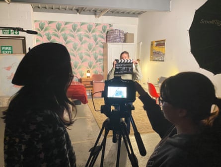 People look through a viewfinder at a person holding a clapperboard