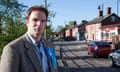 Dr Dan Poulter seen in a village street on a sunny day and is wearing a tweed jacket and blue shirt with a blue Conservatives rosette on his lapel
