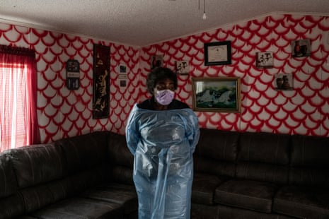 Woman in blue PPE stands in front of a brown sectional couch and pink and white wallpaper