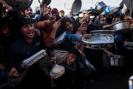 Palestinians hold out tins to receive food at a soup kitchen in Khan Younis
