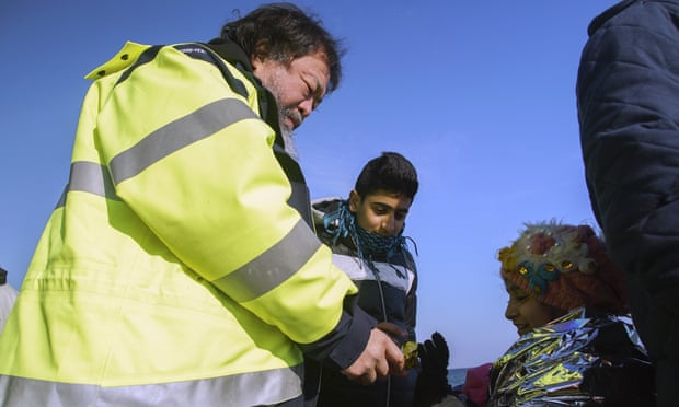 Ai Weiwei gives a chocolate cookie at a girl after her arrival with other asylum seekers on Lesbos.