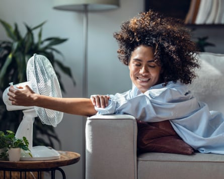 A young woman cooling off using electric fan lying on sofa at home