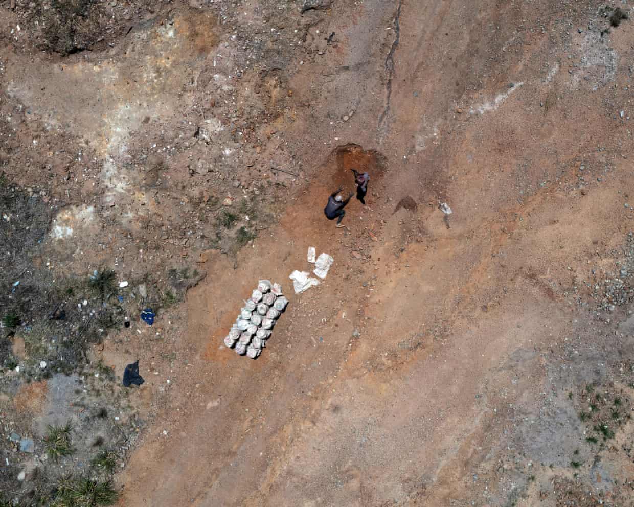 Aerial view of miners digging a hole beside bundled white sacks