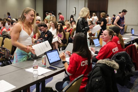 A woman holds a document at a table where women sit with laptops open