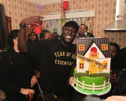 Stormzy and friends in a ‘kitchen’ with extractor fan and magnetic letters, and 1970s wallpaper, drinking out of plastic cups