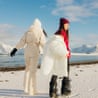 Two Cheerful Women Admiring Nordic Winter Walking at Scenic Beach on Lofoten IslandsRear view of two handsome happy female friends holding hands and running at majestic beach with snowcapped Mountain View under Arctic sun on Lofoten Islands, Northern Norway