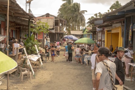 People on a small sandy road lined with small shops and restaurants with wooden walls and corrugated metal roofs