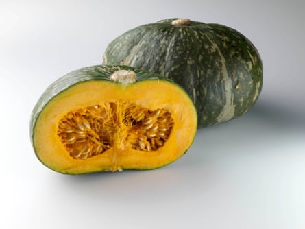 One full green squash, and one half, with the bright orange center facing the camera, on a white table.
