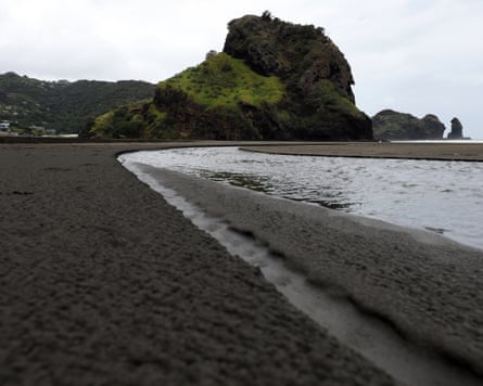 The black sands at Piha, the waves lapping the shore, with a green hillock in the background