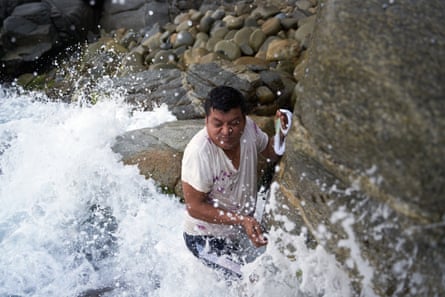 A man stands waist-deep in the surf next to a rocky shore
