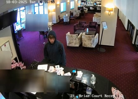 A screengrab from security video shows Natland, who is wearing a black hoodie with hood up, standing at a hotel reception desk while the receptionist handles banknotes. There are armchairs in the lounge behind him.