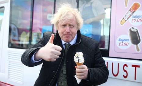 A man in a suit holds an ice cream in one hand and makes a thumbs-up gesture with the other