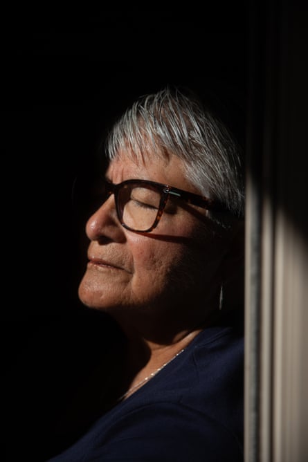 Close-up portrait of woman with short gray hair and glasses leaning head against doorframe, eyes closed, half her face in bright sunlight and the other completely in shadow.