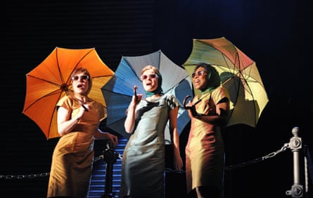 Three women holding colourful umbrellas on stage.