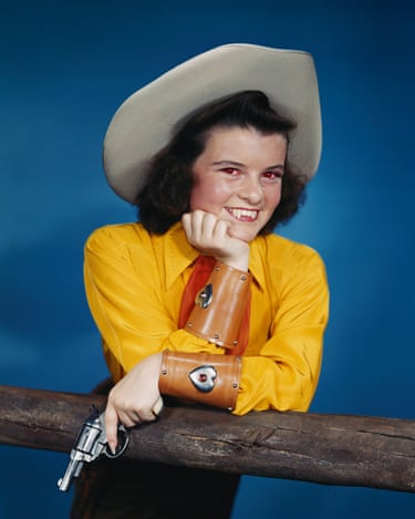 Colour photograph of a woman in cowboy attire posing with a gun in her hand. In the picture you can also see she has extended incisors and reddened eyes