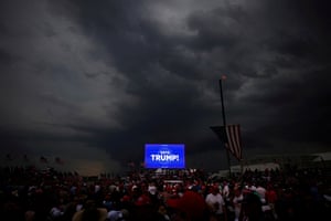 Storm clouds hang over a crowd in front of a screen with the message 'vote Trump'