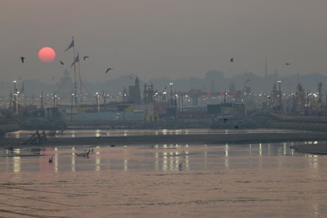 The sun sets on a misty riverside scene dotted with strings of electric lights on poles