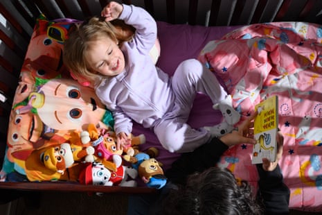A mother reads to a young girl in a crib wearing a purple onesie