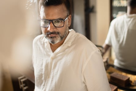 A man in glasses and a cream top looks solemn.