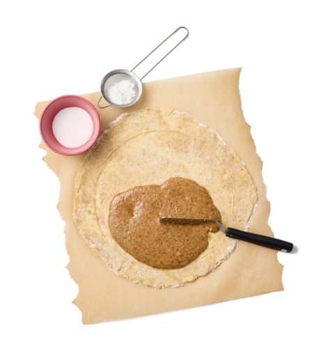 Flat pastry on a baking sheet with baking utensils and jam spread.