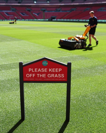 Groundsmen mow the pitch in front of a ‘Please keep off the grass’ sign