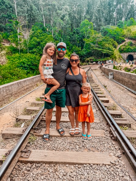 A man and woman with their two children, standing on a railway line in Sri Lanka, trees behind them