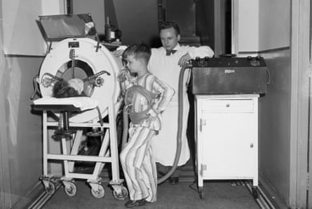 a child stands by a woman inside a piece of medical equipment as a doctor looks on