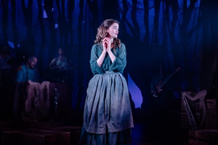 A woman stand looks concerned in a spotlight on stage