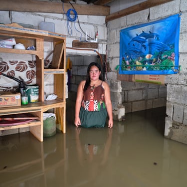 A woman stands in a flooded room next to wooden shelves and a picture of an underwater scene