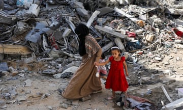 A woman and child walk among debris, in the aftermath of Israeli strikes on Nuseirat refugee camp
