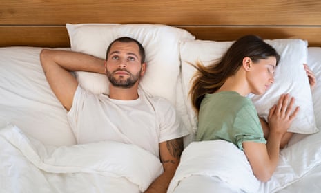 Man awake in bed next to sleeping woman.