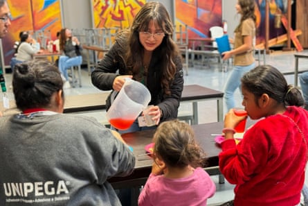 a woman pours a drink from a pitcher into a cup for three people seated at a table