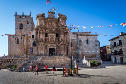An ornate church facade and square in a Spanish village with children playing.