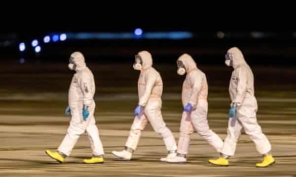 Health officials walk on the tarmac as they prepare for the arrival of five Czech and two Slovak nationals who were evacuated from Wuhan